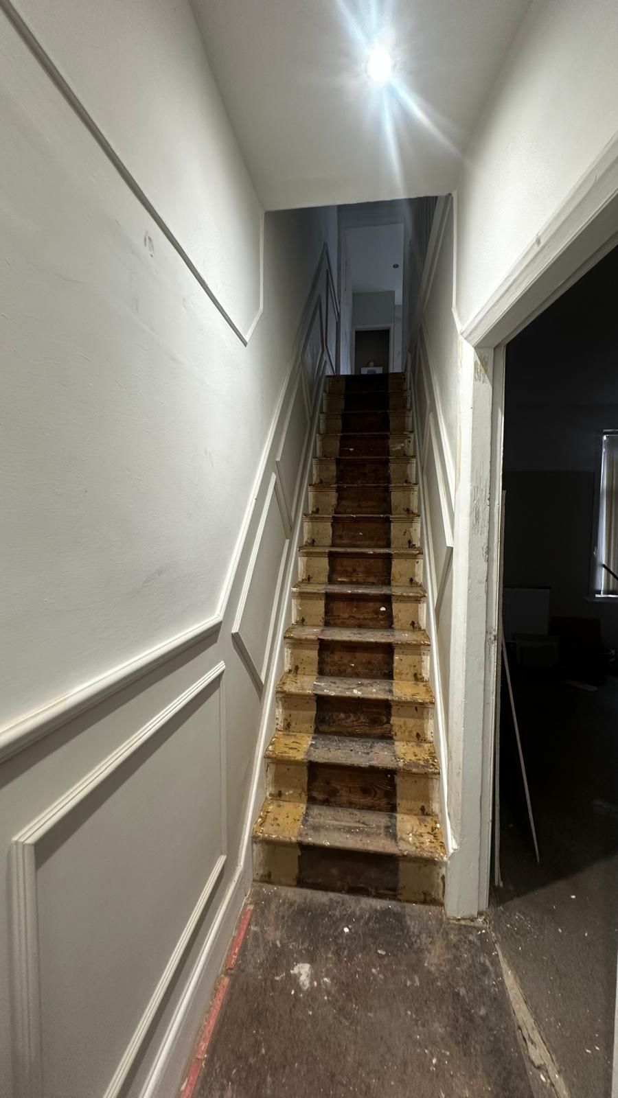 Bare, paint-stained staircase and dirty hallway floor