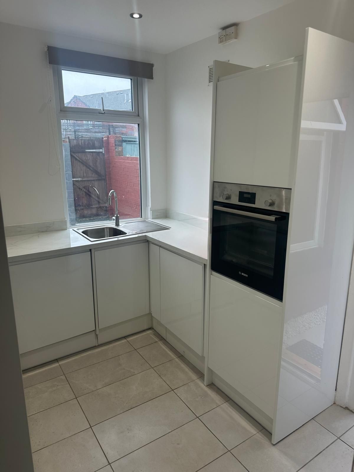 New white gloss handleless kitchen with marble-effect worktops and built-in Bosch oven